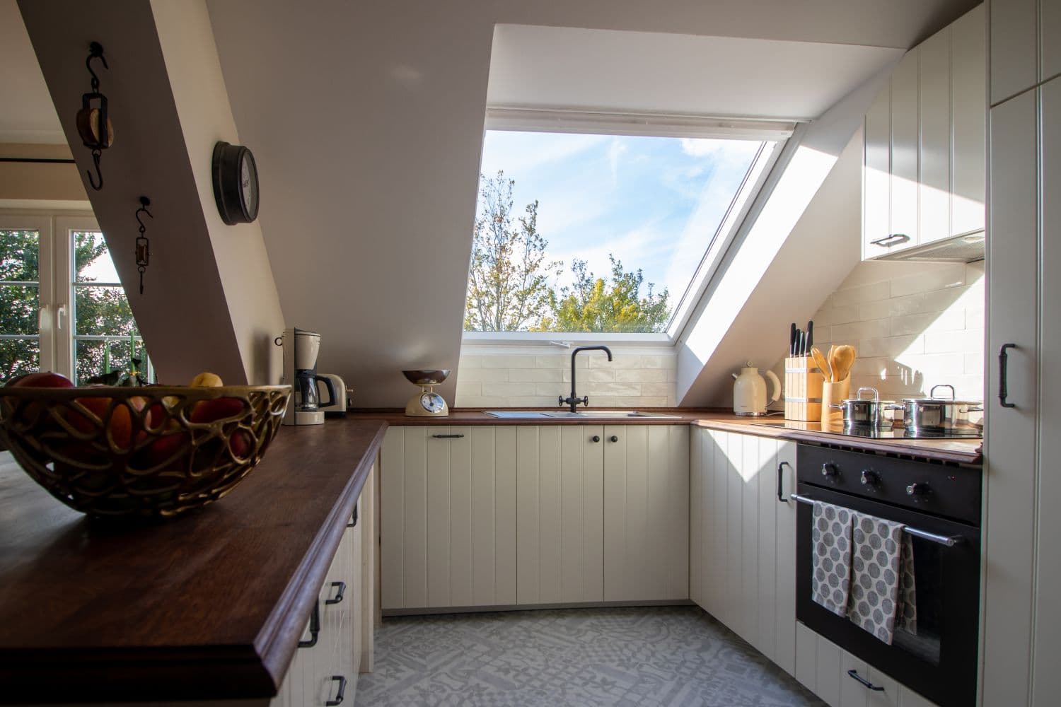 U-shaped kitchen with cream fronts, wooden worktop, a roof window above the sink and an oven with tea towels