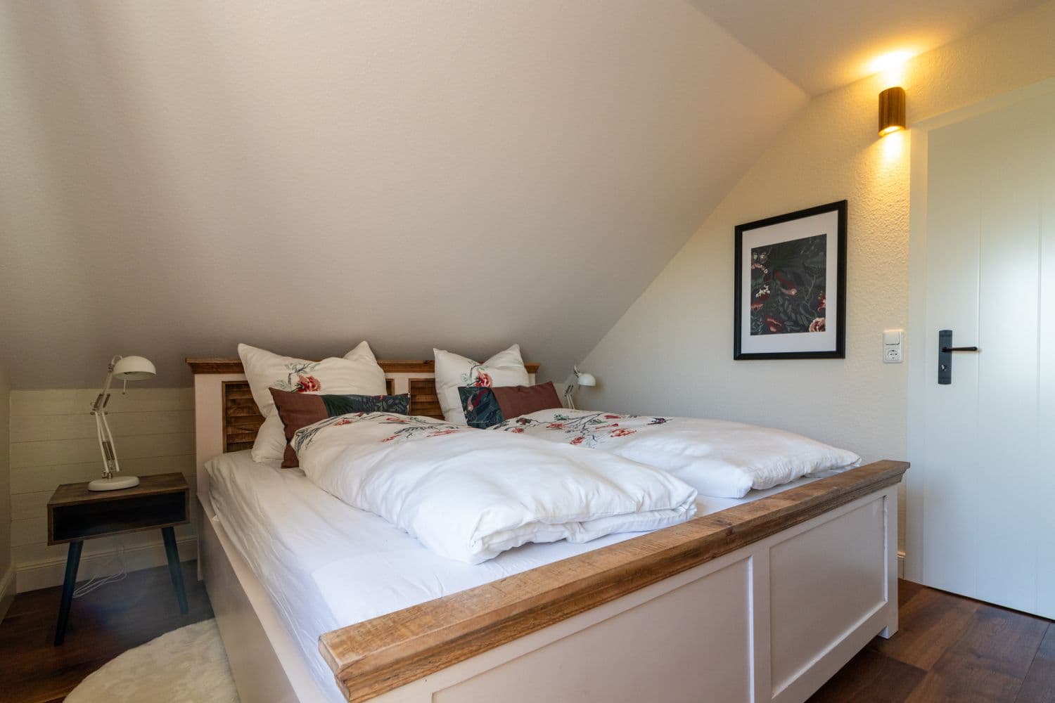 Second bedroom with a double bed, white bed linen with a flower motif, a wall lamp and a framed picture on the sloping ceiling