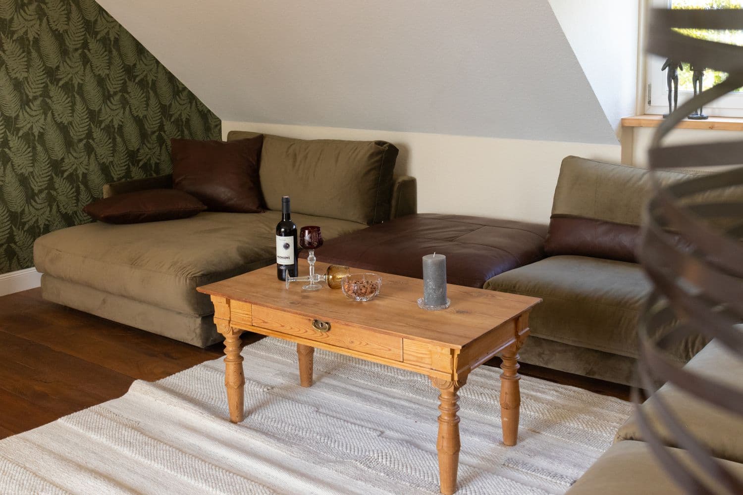 Pine coffee table with a bottle of wine, a glass of red wine and a bowl of nuts in front of the corner sofa